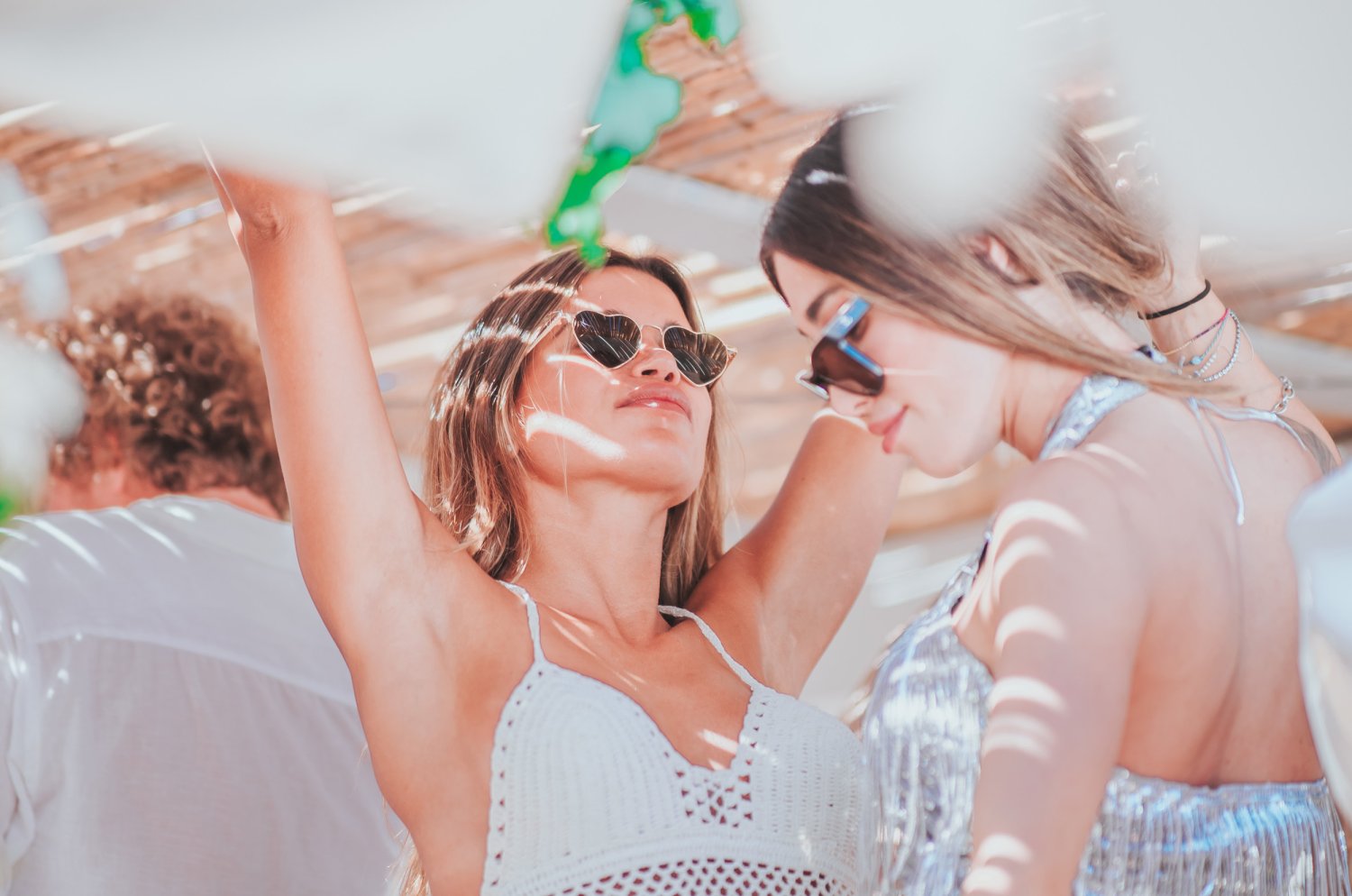 Women wearing sun glasses with arms up in the air, dancing