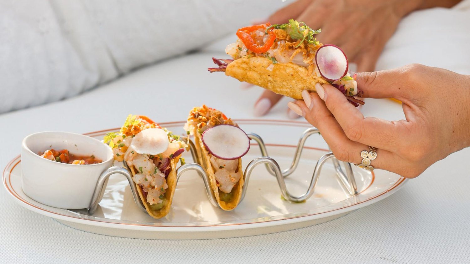 someone picking up a crispy taco from a plate of tacos