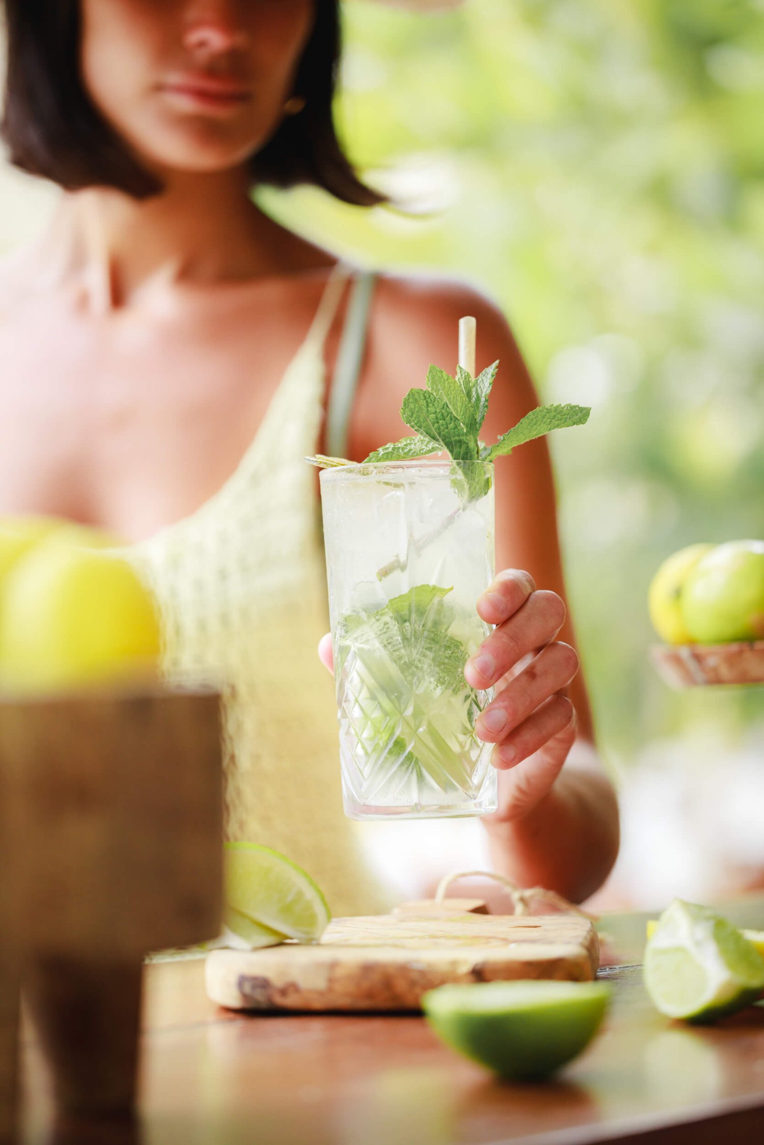 A women holding a glass of mojito, garnished with mint. A freshly cut lime lays on the table next to the glass