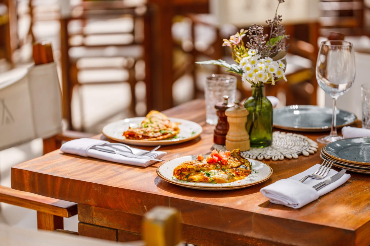 a set dining table with two dishes placed, cutlery sits within a folded napkin next to the plates