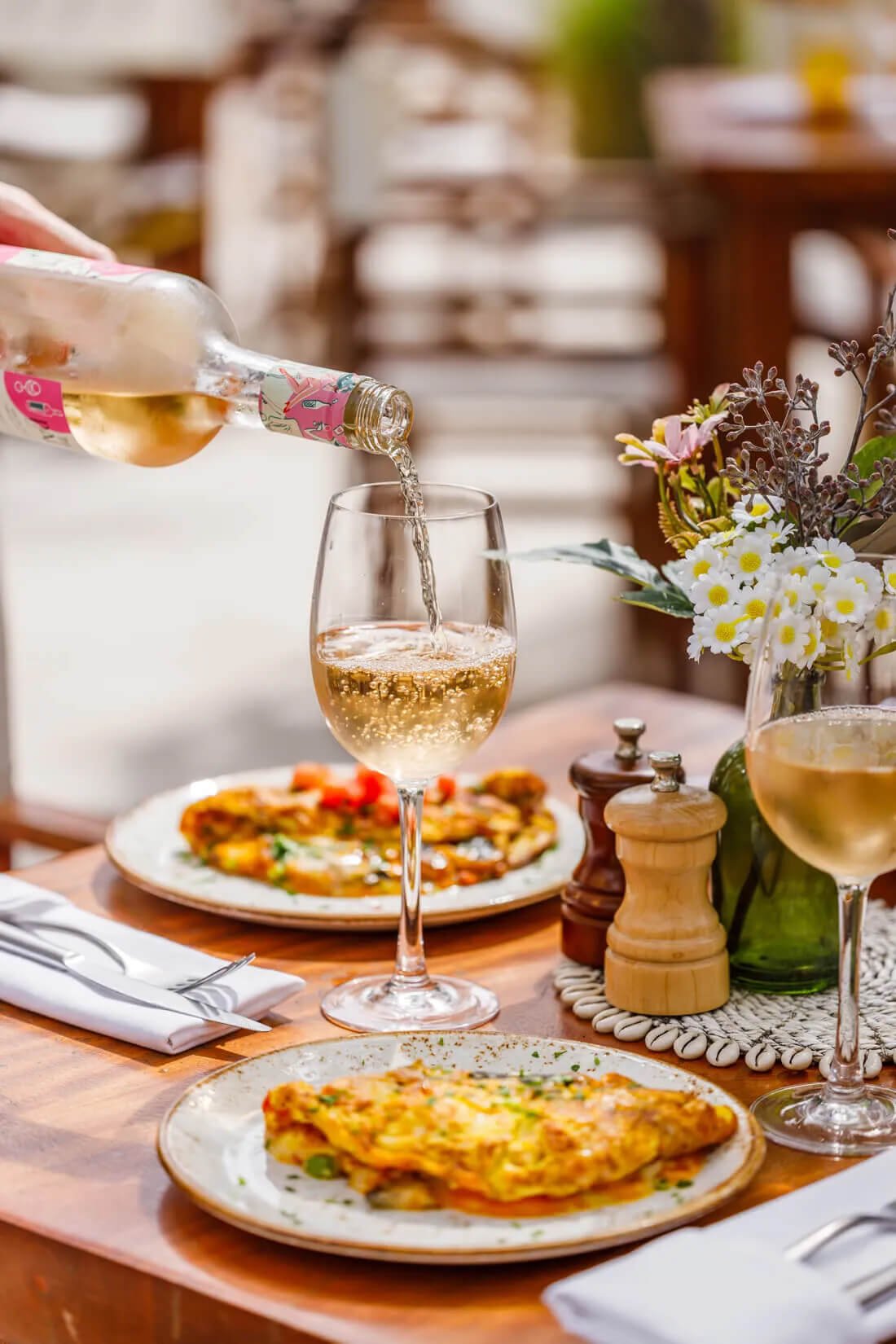 a table set with dinner, flowers at the centre of the table while someone is pouring a glass of wine