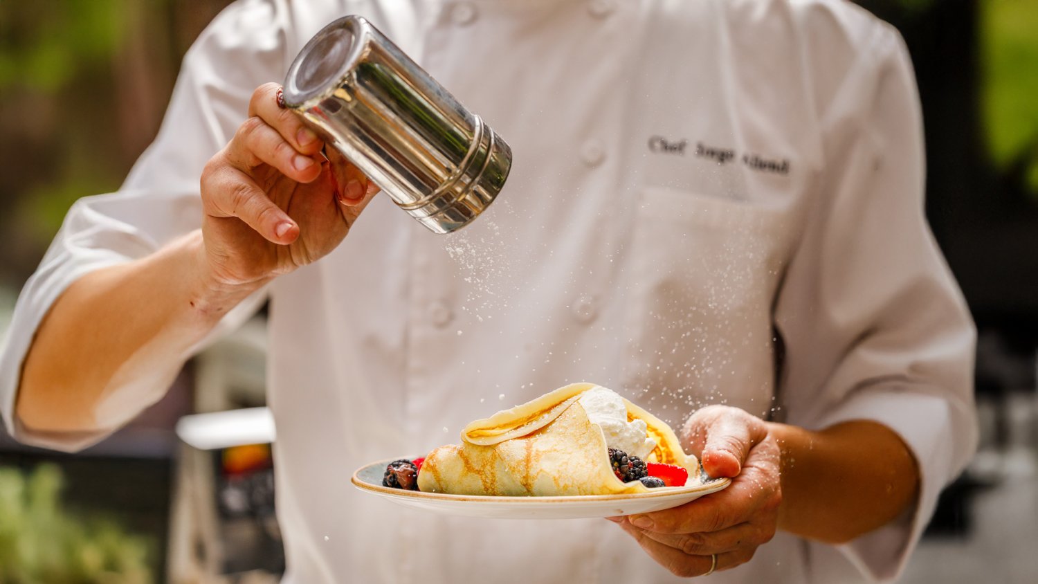 A chef sprinkling sugar over a crepe
