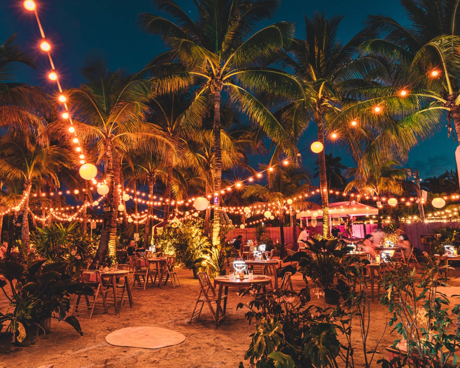 Nikki Beach Miami - The Northside Oasis. A private outdoor beach dining events area. Lit by fairy lights hung between palm trees, dining tables on the sand nestled around plants