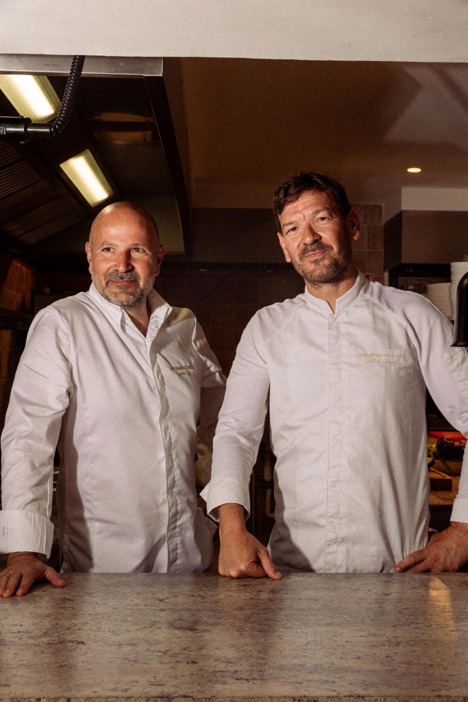 Two chefs posing for the camera, leaning on a counter
