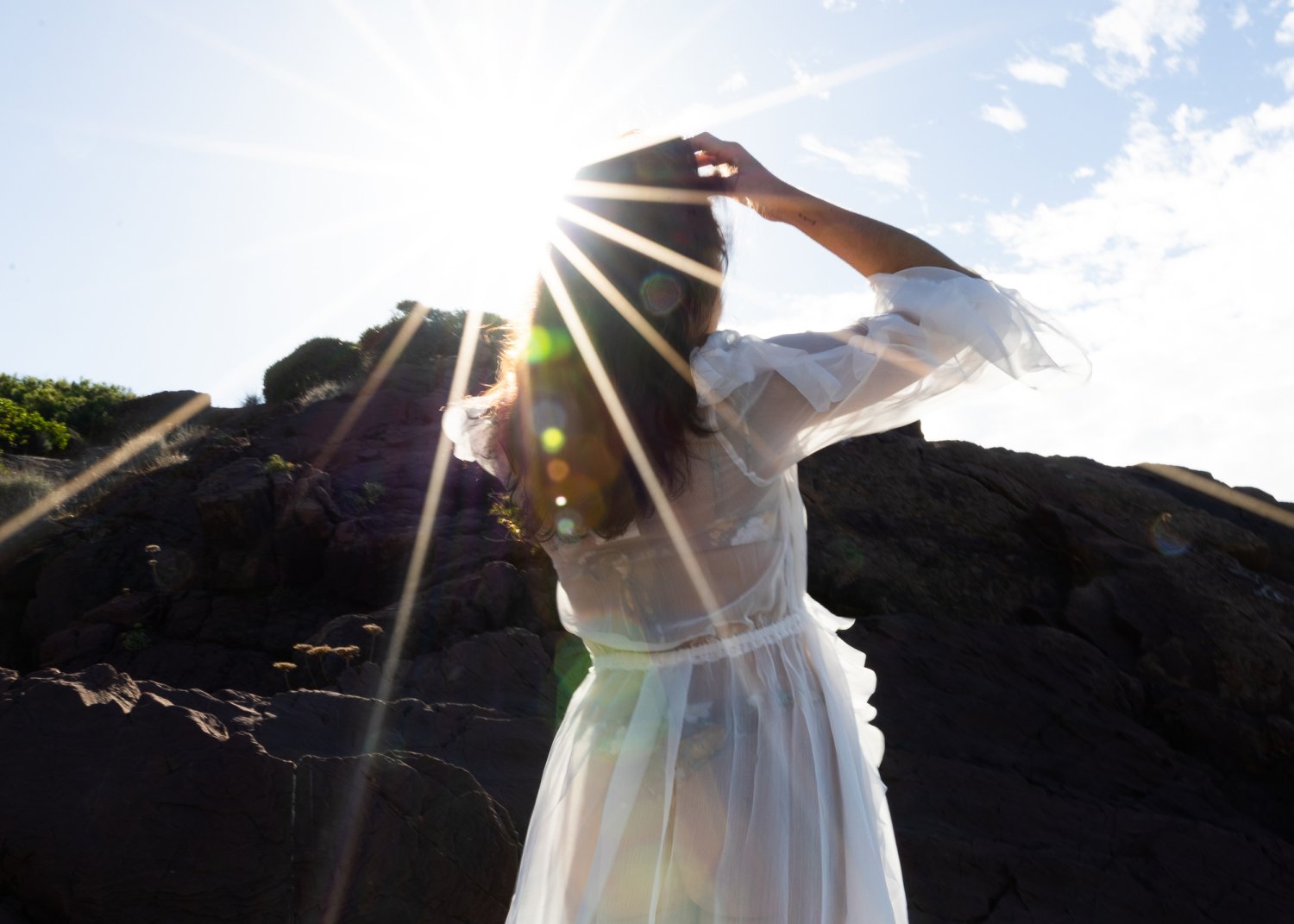 A lady standing in the sunlight in a flowing white beach cover up dress