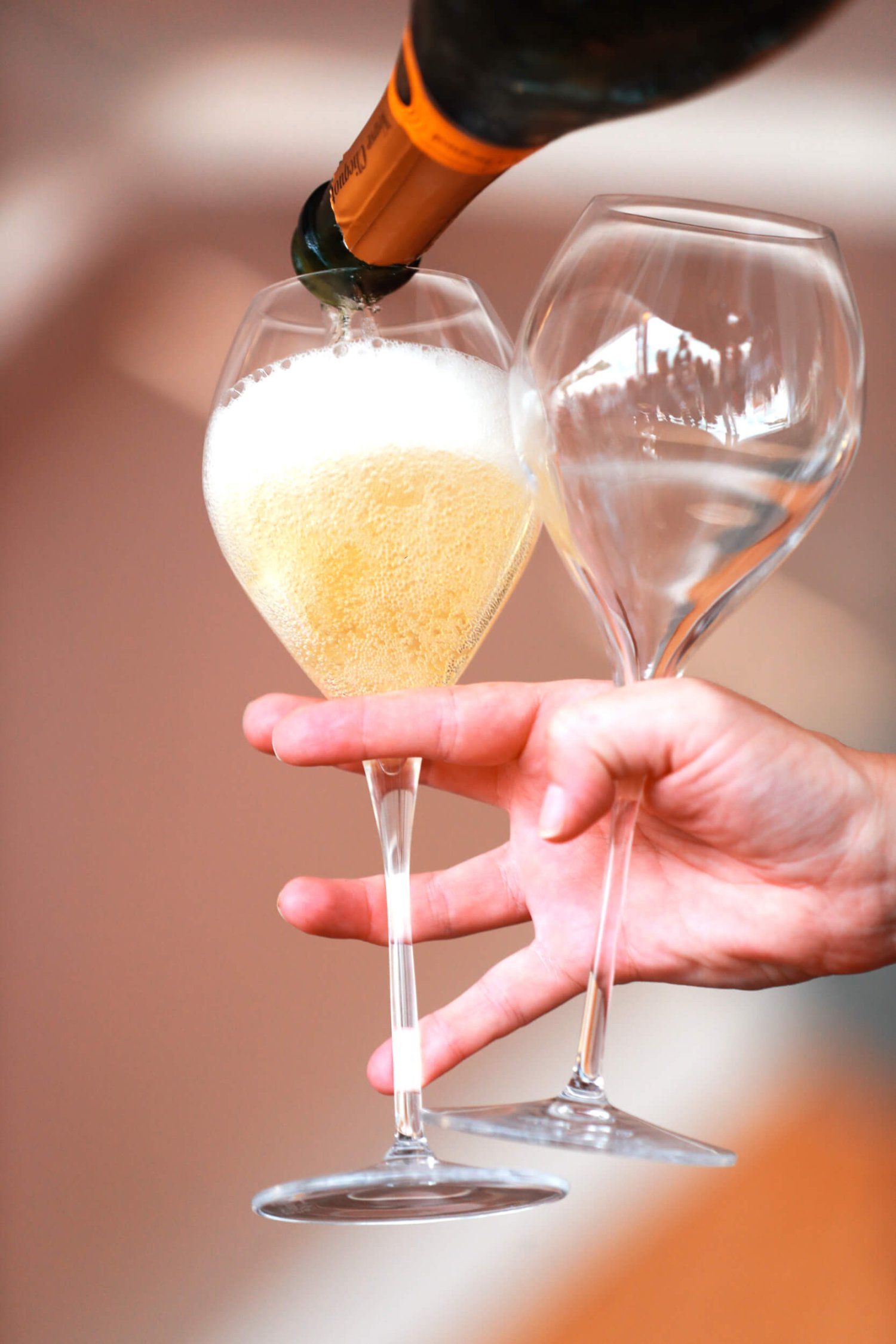 Close up angle of someone holding two wine glasses in one hand while pouring a of sparkling wine with the other
