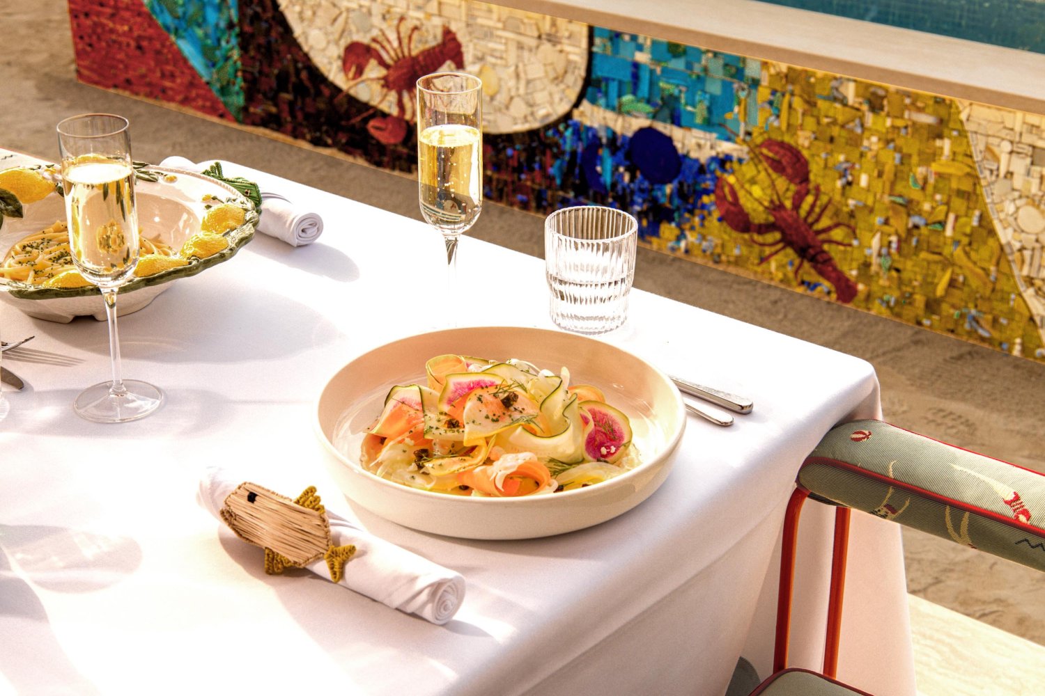 Close up image of dining table with pasta dish and salad dish, served with glasses of Prosecco