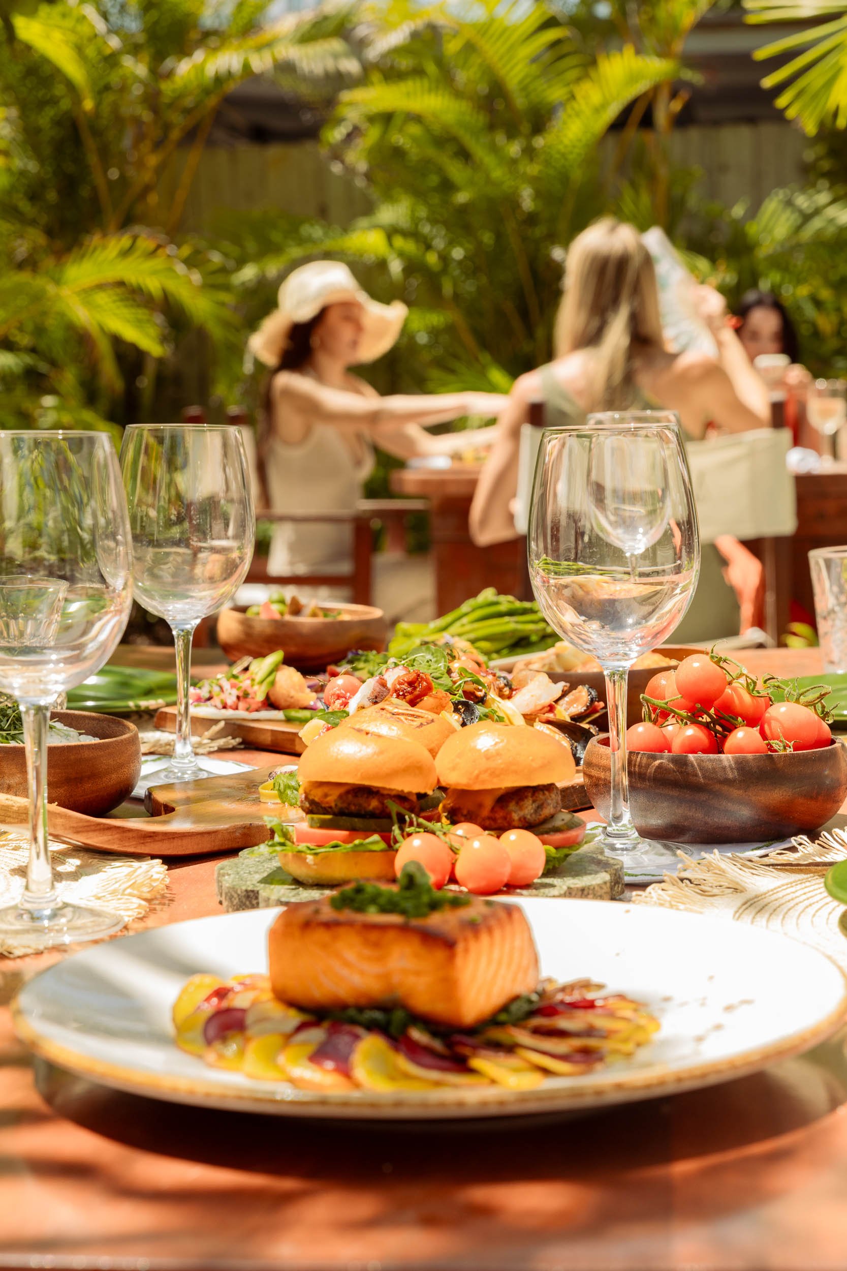 A table spread of various Nikki beach dishes including burgers and a plate of salmon