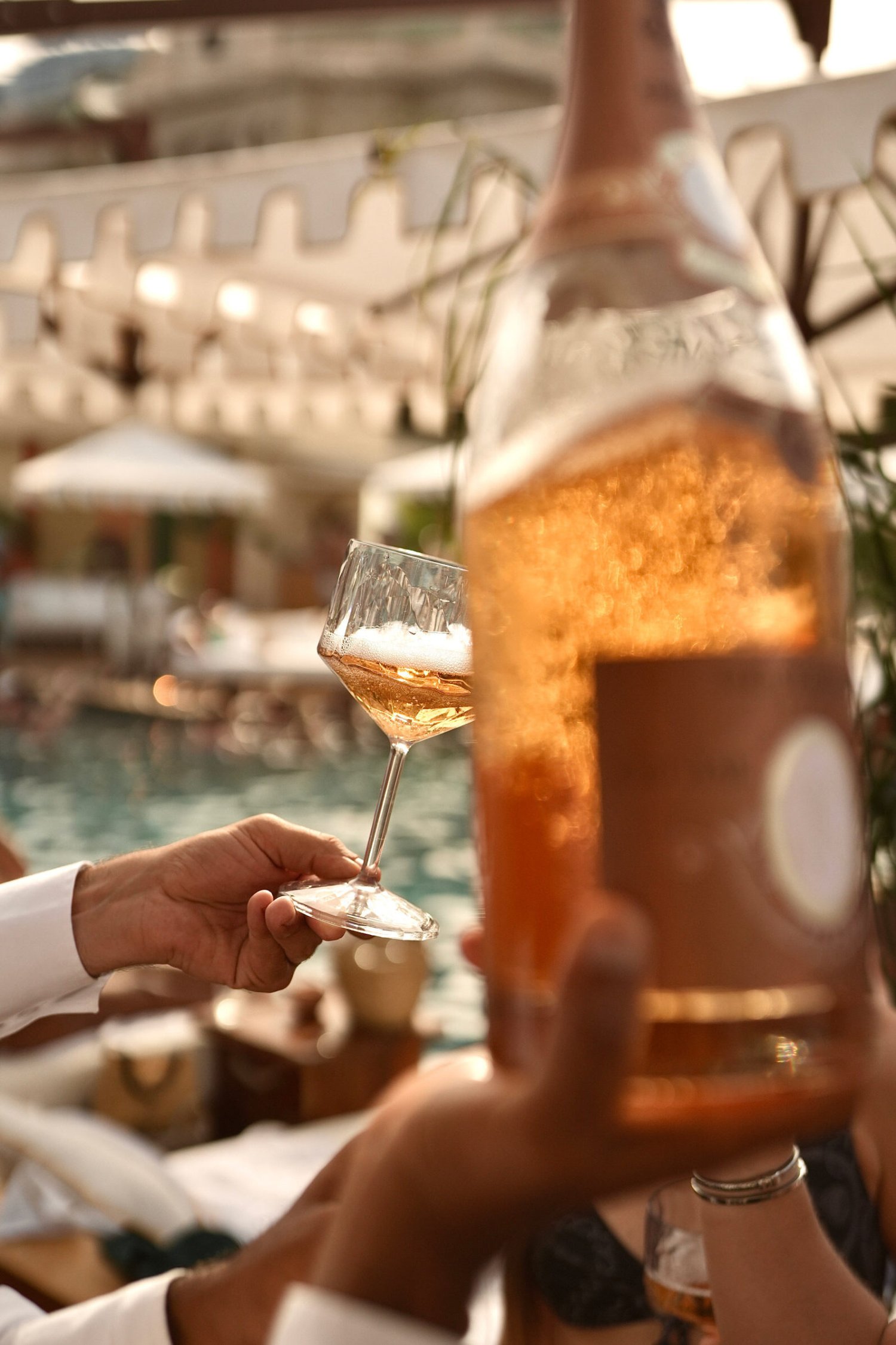 A waiter holding the base of a wine glass and holding a wine bottle by its base in the other hand