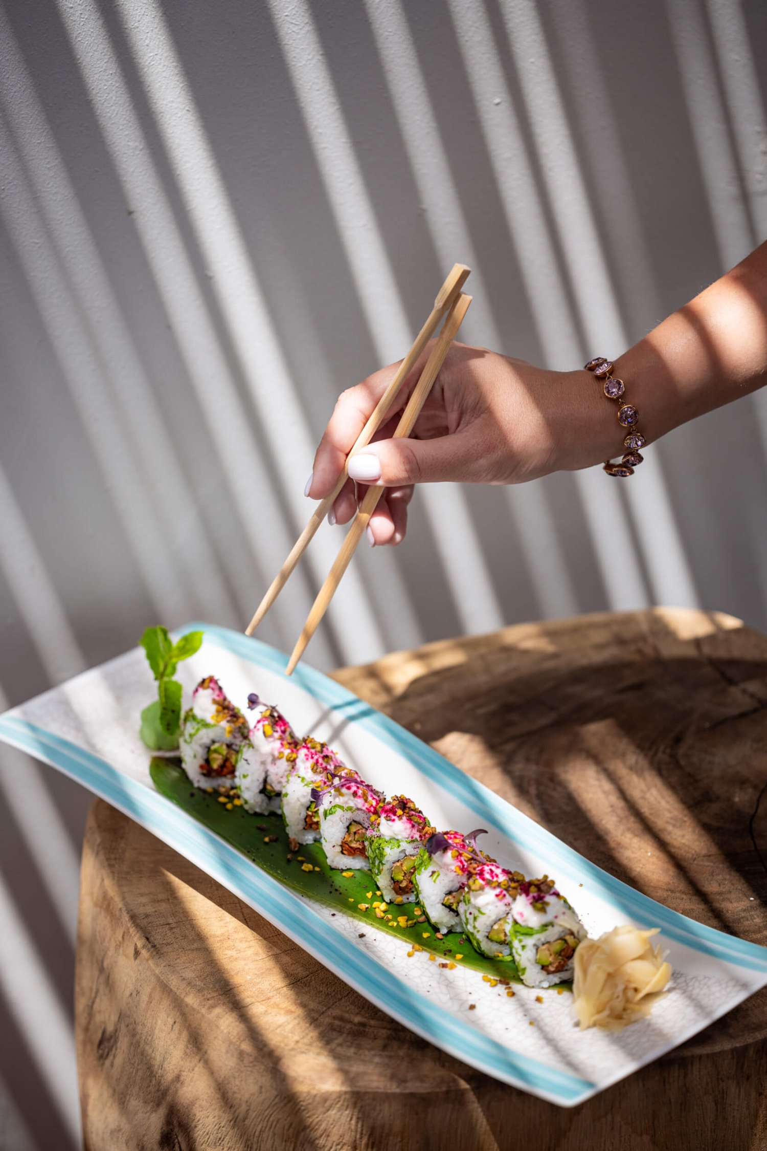 A platter of sushi with a woman reaching in to pick a piece up with chopsticks