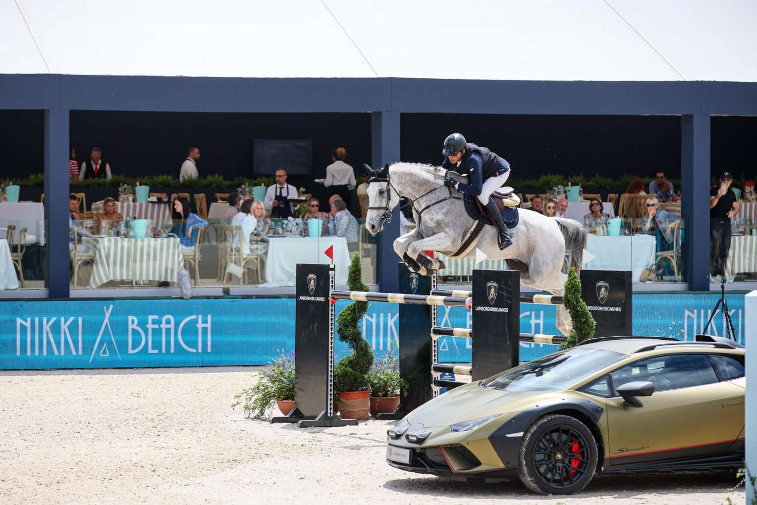 Horse and jockey jumping a hurdle next to a lamborghini