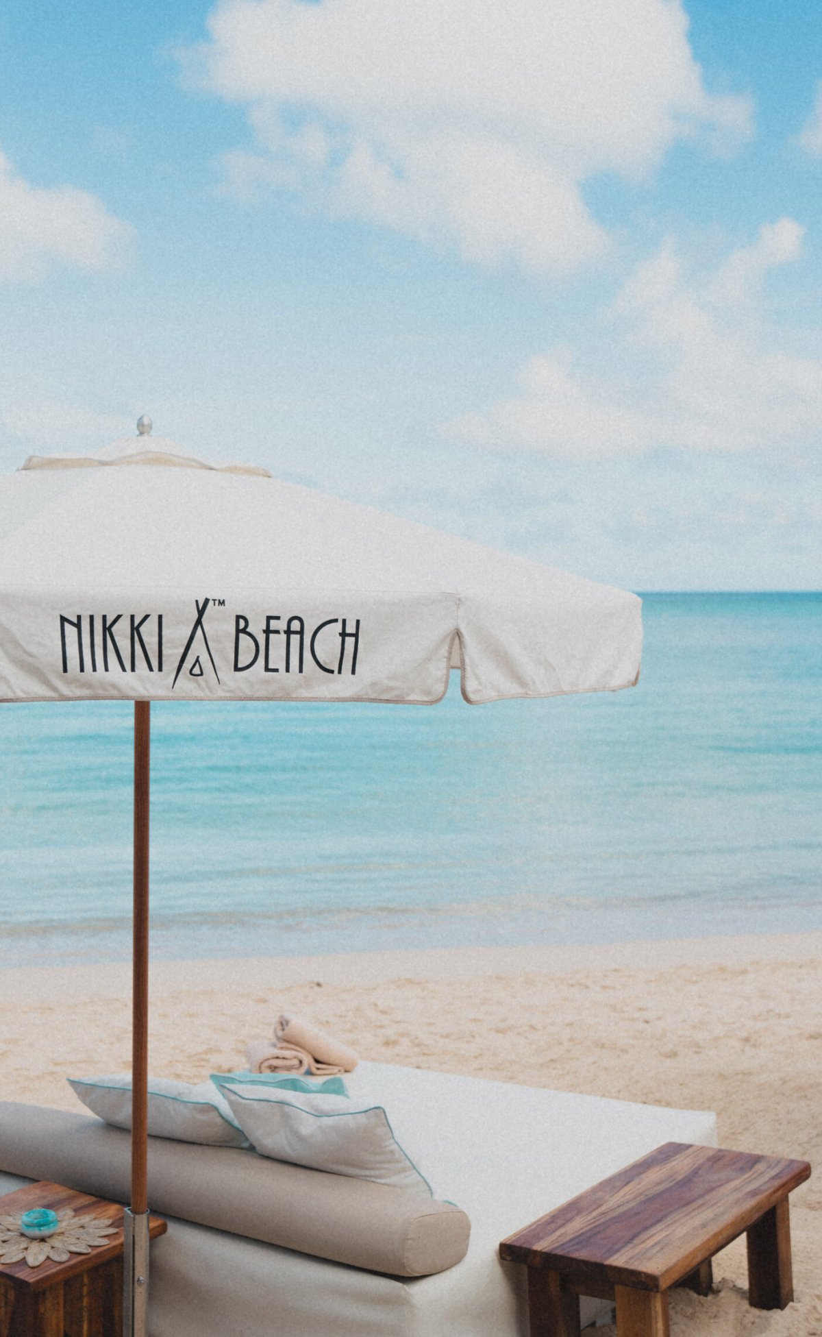 Branded Nikki beach umbrella on beach with sun bed and beach towels