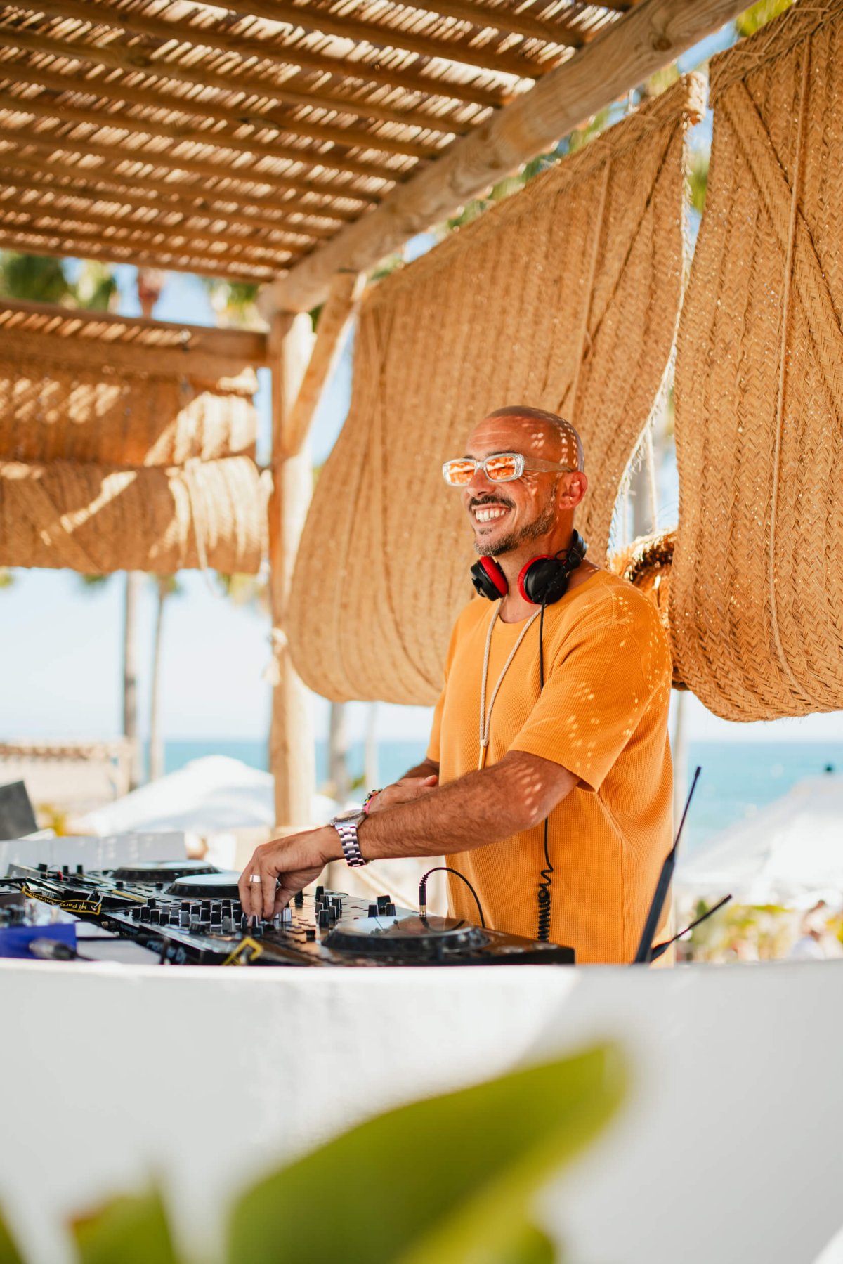 A DJ smiling wearing headphones around his neck in a yellow shirt