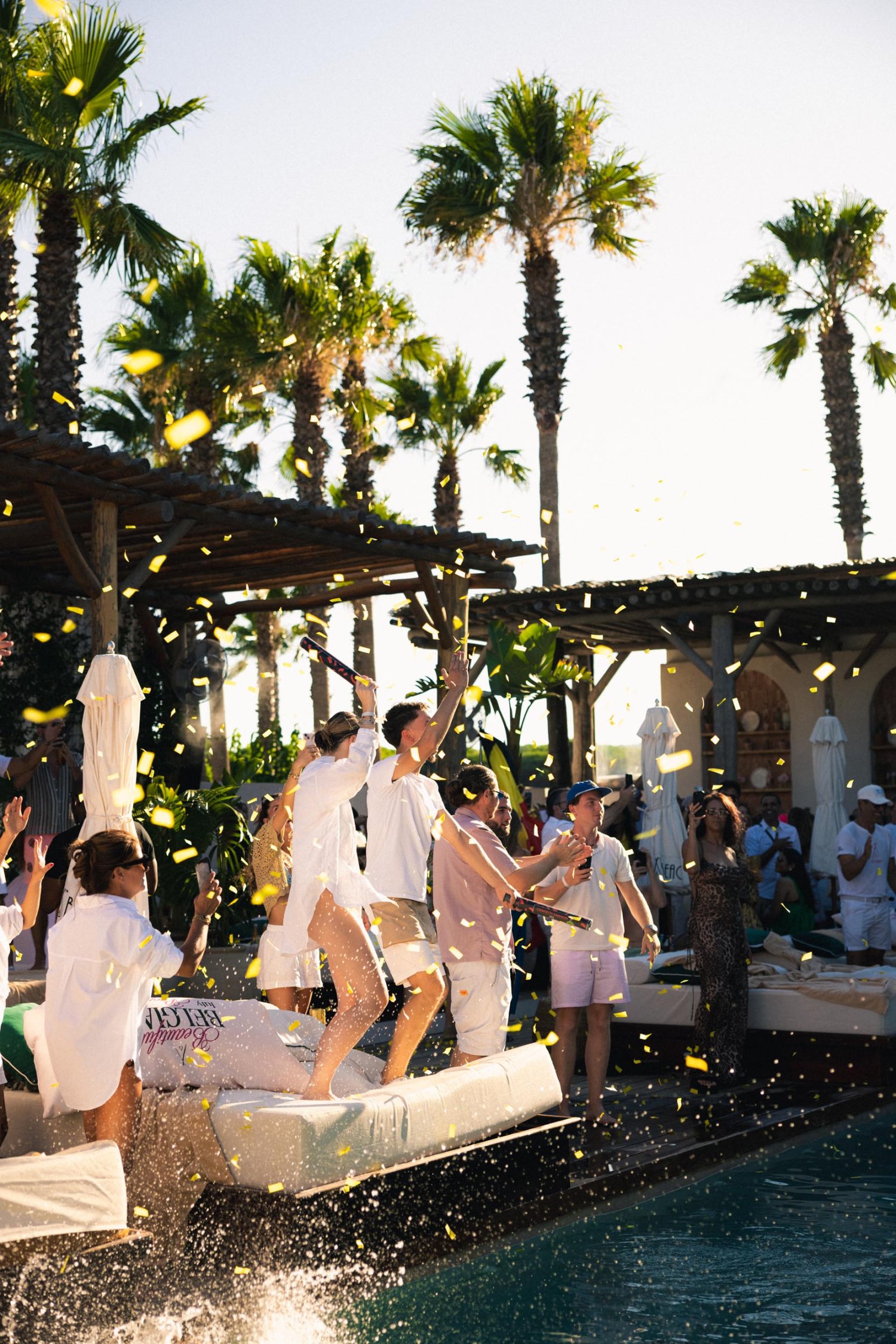 Group of individuals dancing and celebrating on the poolside, setting off confetti cannons