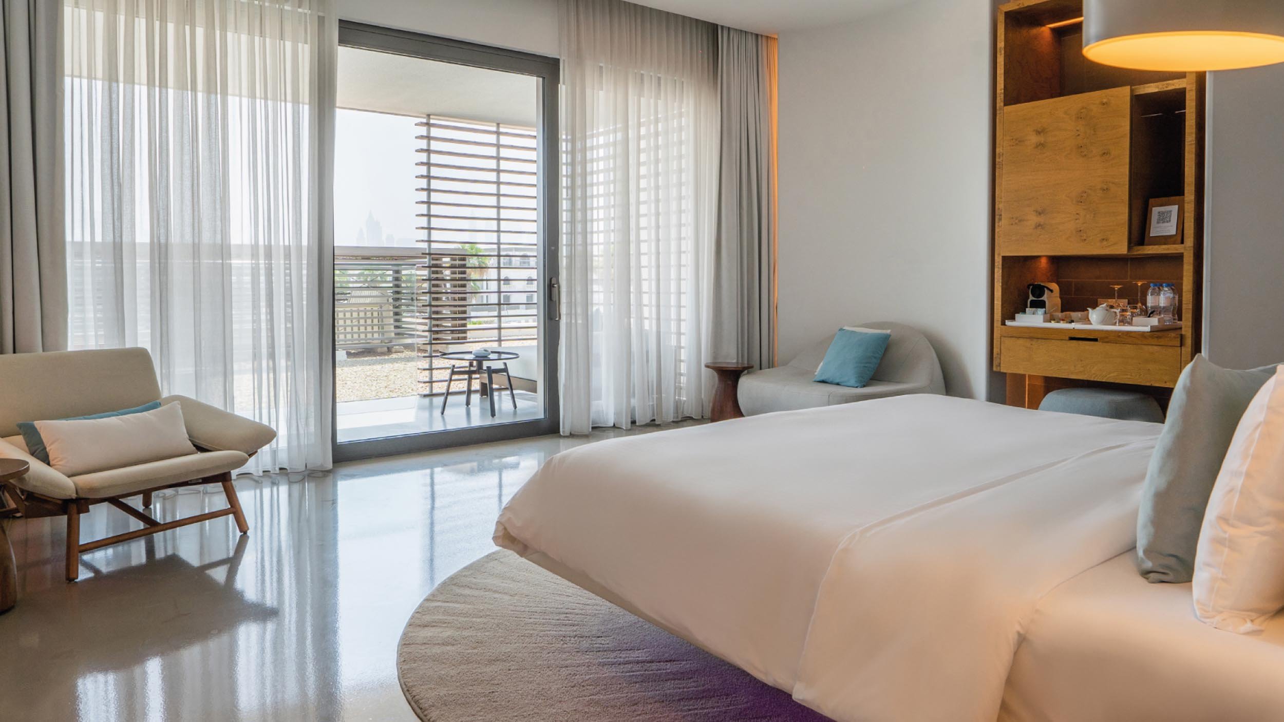 King sized bed and arm chairs with a small counter of glasses, water and coffee