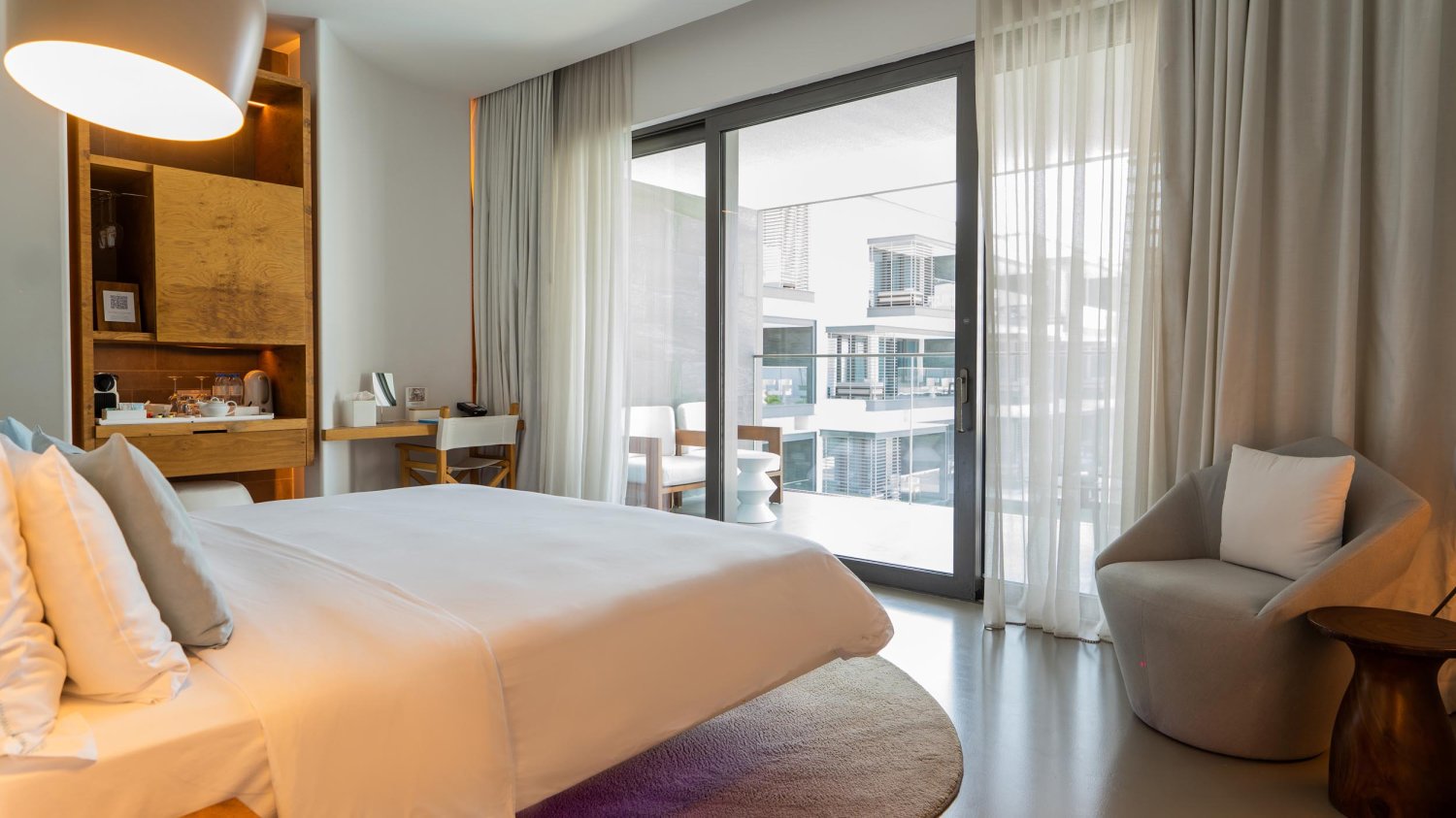 King sized bed with a small counter of glasses, water and coffee, a dressing table and arm chair
