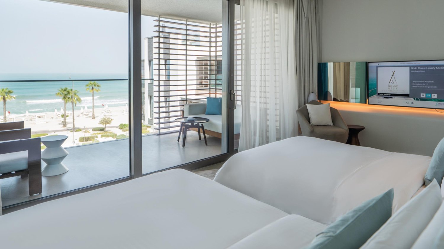 Two single beds next to flat screen tv, looking out to the sea view balcony