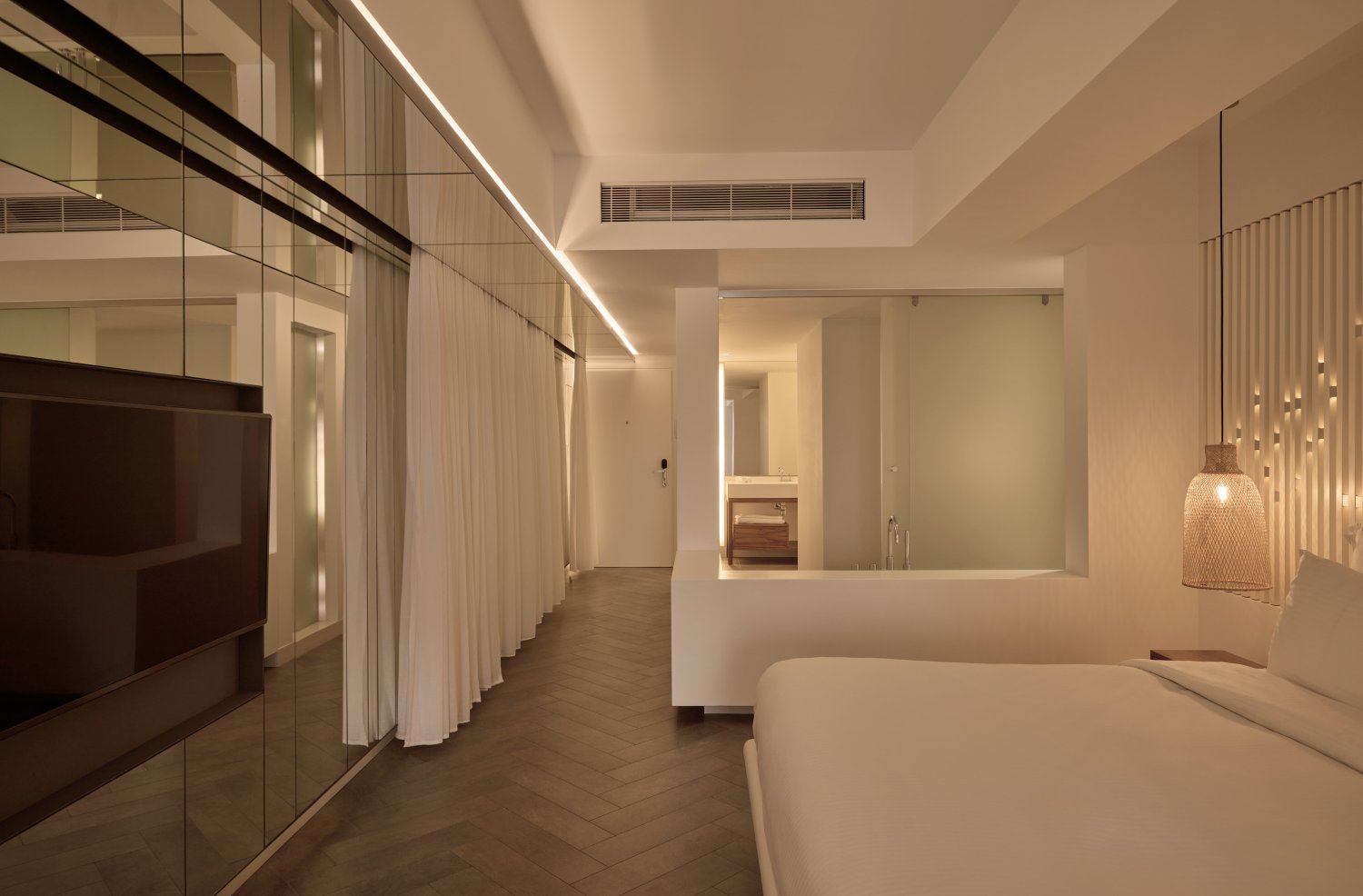 A luxurious room featuring a plush bed, a sleek television, and an elegant mirror reflecting the sophisticated decor