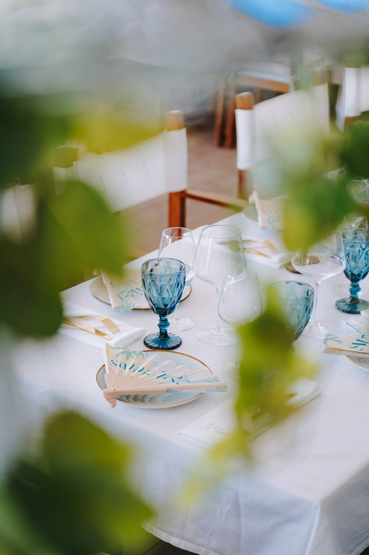 White table with blue glassware with leaves out of focus in the foreground
