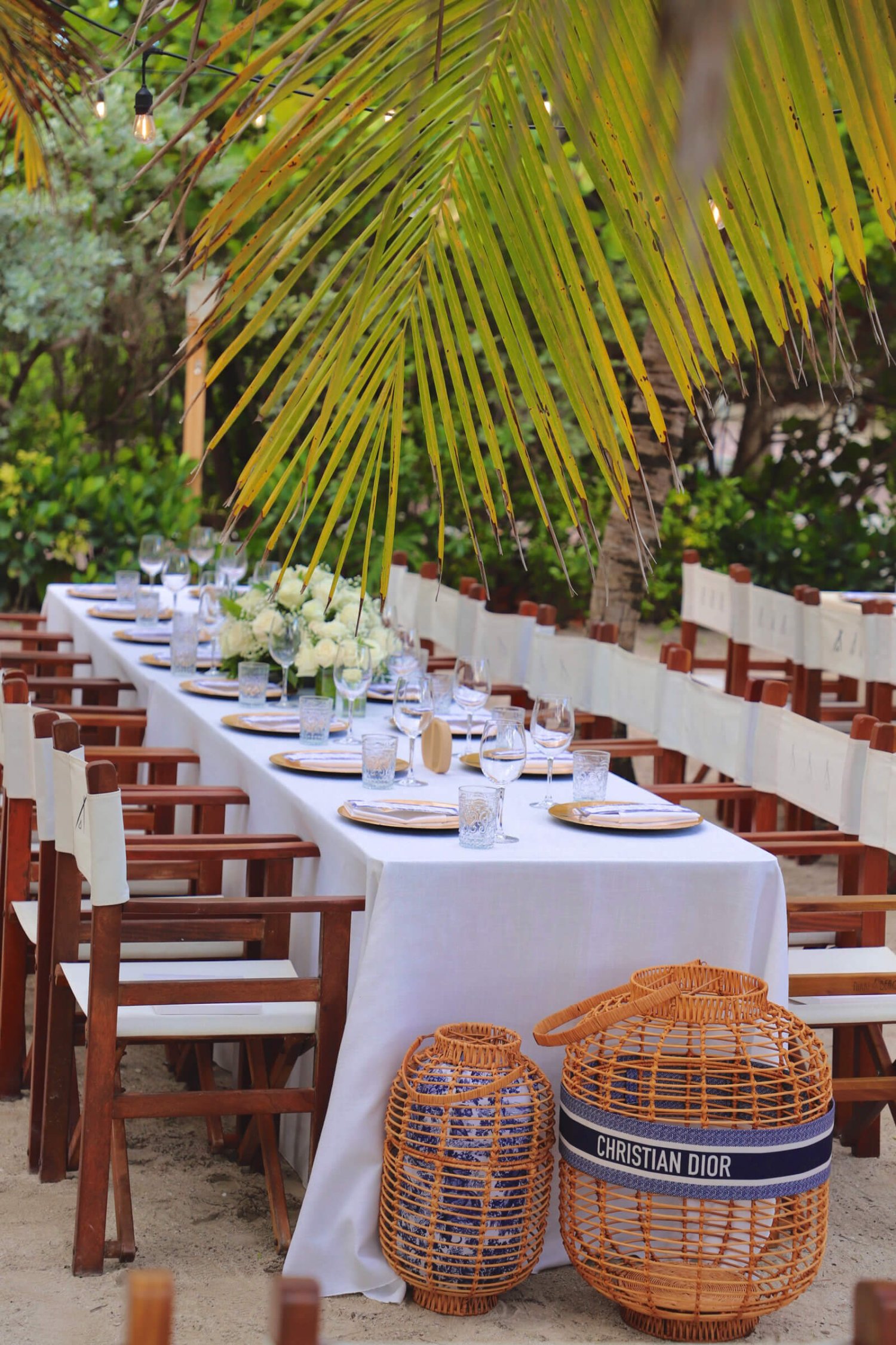 A long dining table set ready for guests, seating approximately 20 people. A Christian Dior wicker basket sits in front of the table