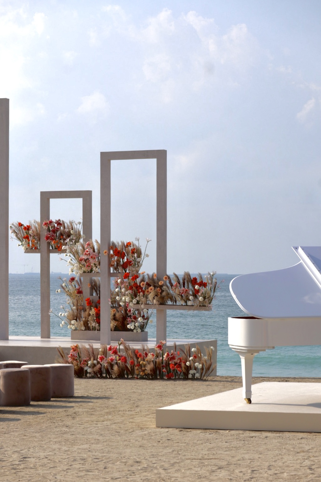 Grand white piano on the beachfront with floral display behind. Sea view in the distance