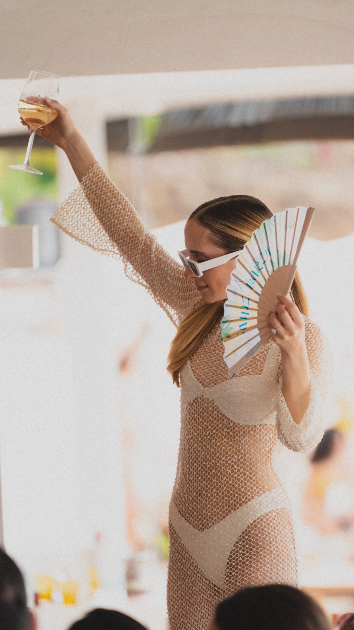 A women standing raising a glass in one hand while holding a fan in the other