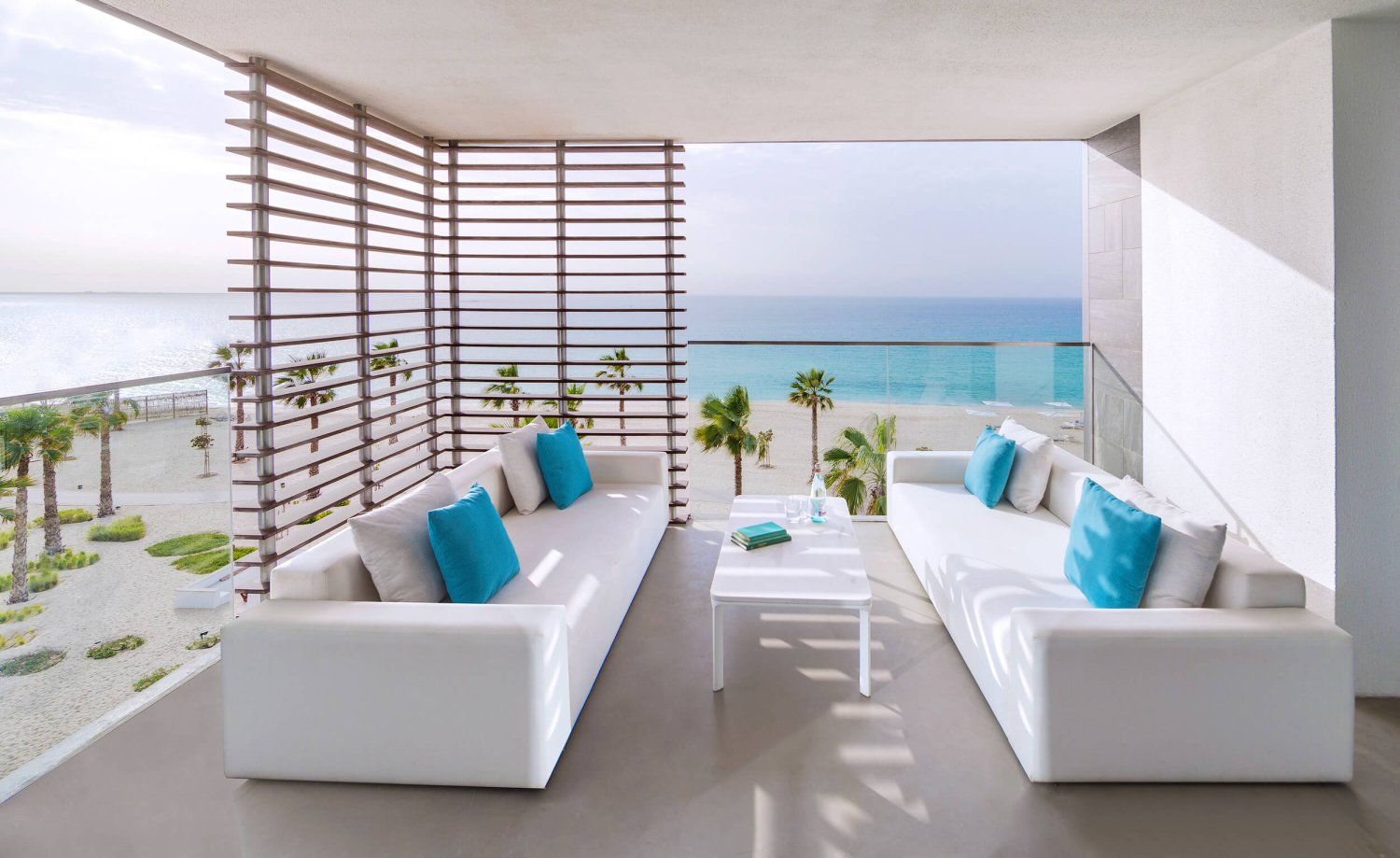 A view of the Luux suite balcony with two sofas, the view overlooks the beach and palm trees