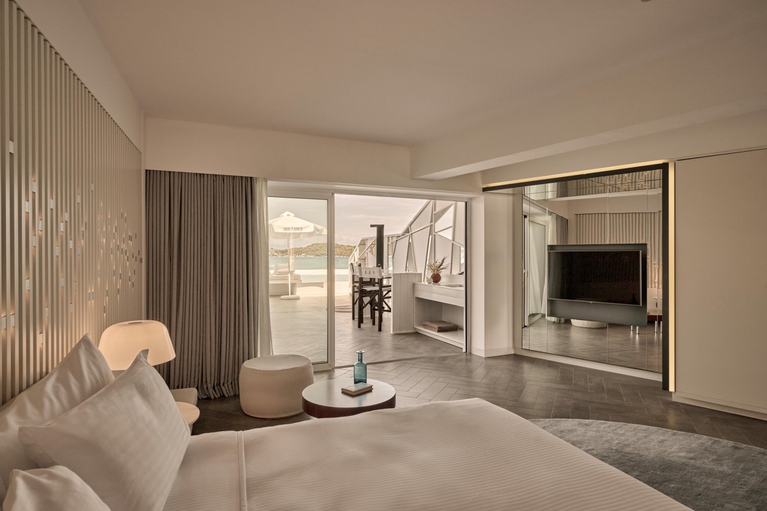 Elegant bedroom featuring a large bed and a television, designed for relaxation and coastal luxury