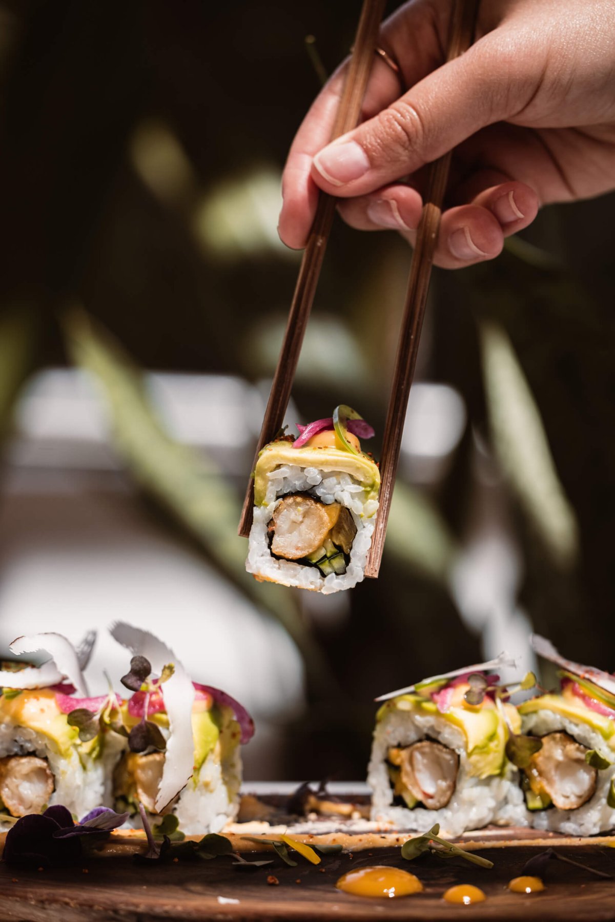 A hand holding chopsticks picking up sushi from a platter