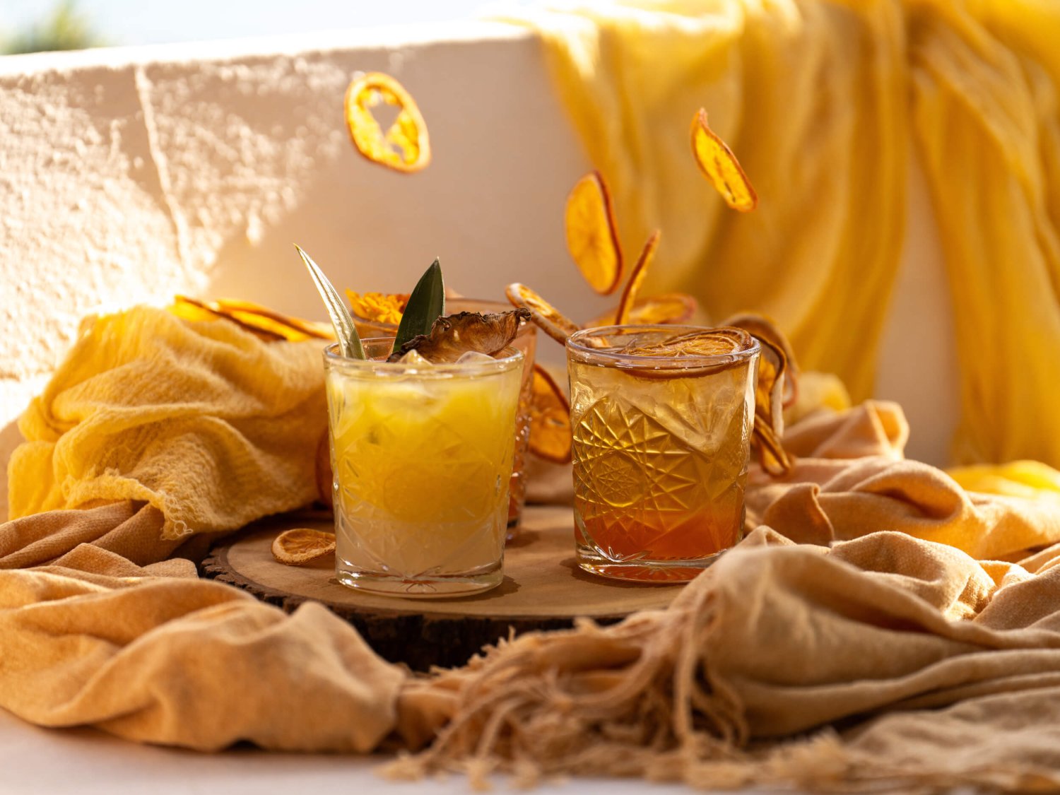 Two cocktails surrounded by a cream cloth with dried fruit falling in the background