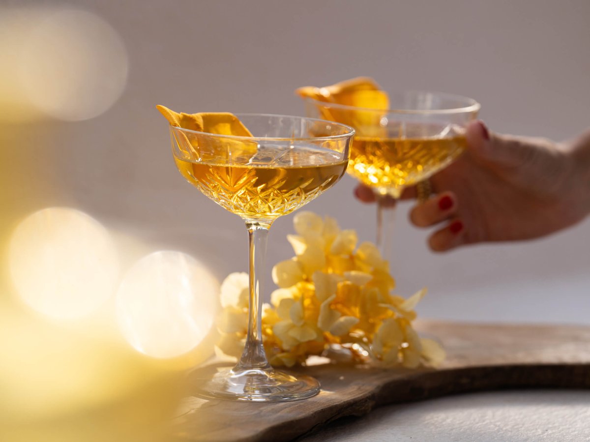 Two cocktail glasses with a woman's hand entering the picture taking one of the glasses