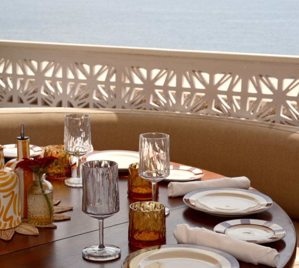A table looking out to the sea, the table is set with plates, cutlery and wine glasses