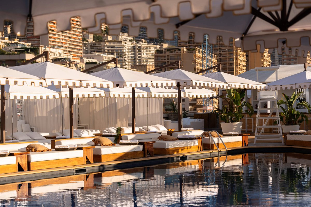 Sun beds with parasols at the side of a pool with buildings in the background