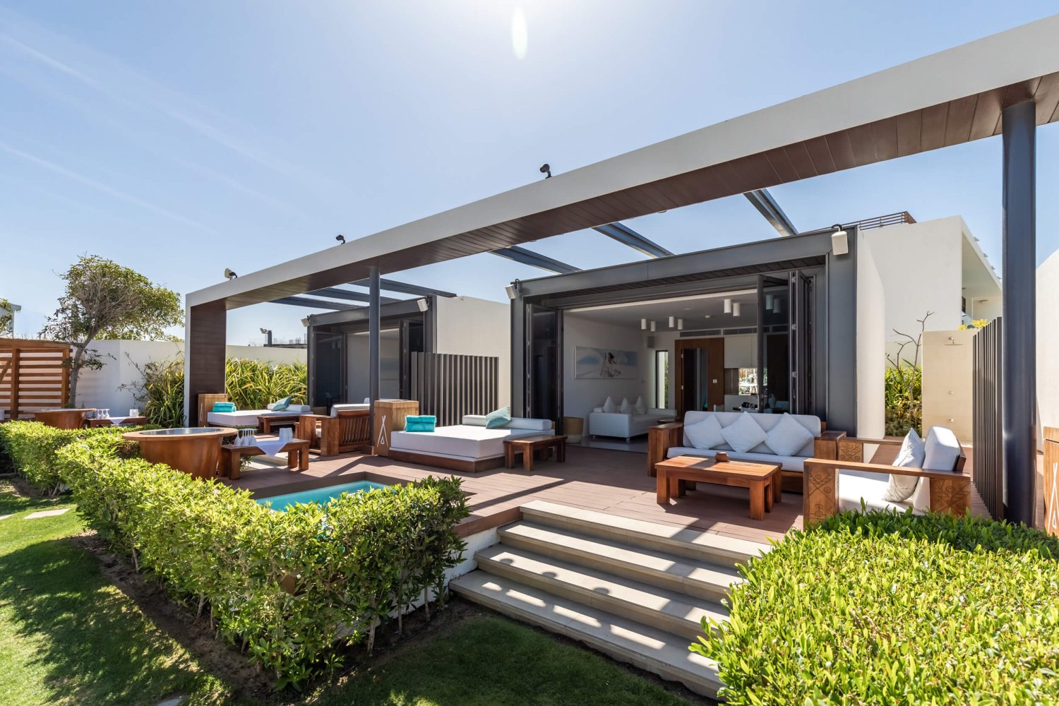 A view looking into the garden villas from outside. Sliding doors are pushed back showing the living room area while outside there are sofas and a small plunge pool