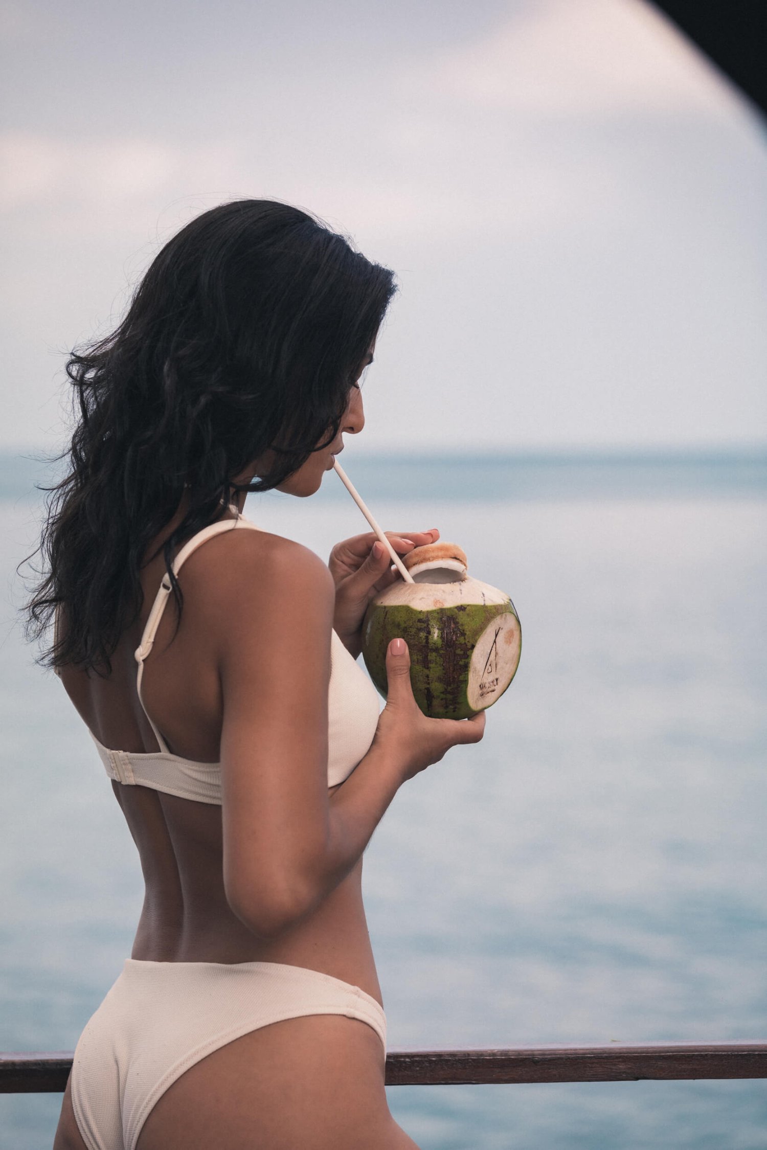 Woman in a white bikini drinking out of a coconut