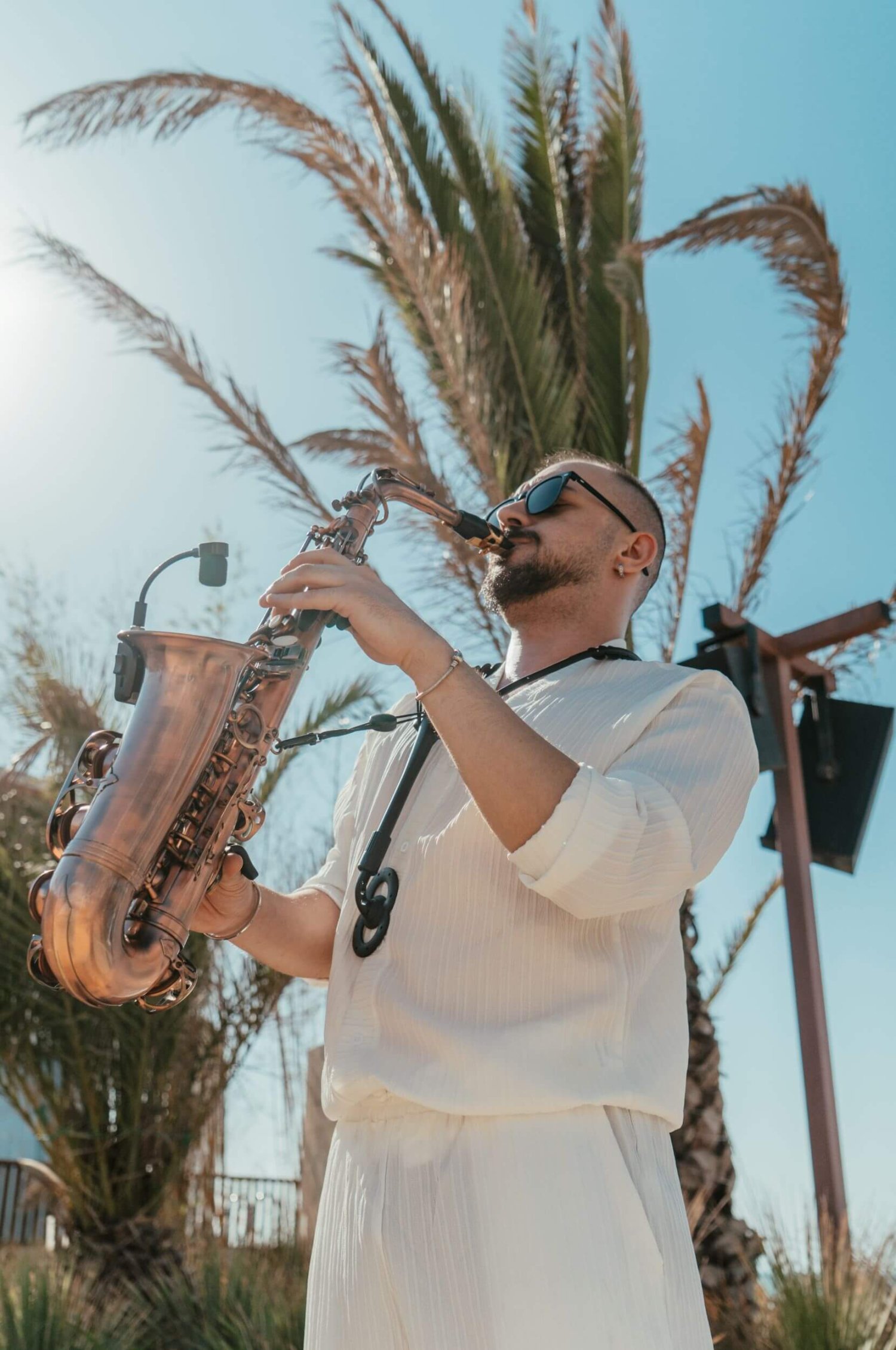 Alt Text: A live saxophonist dressed in crisp white resort wear and sunglasses plays his instrument outdoors against a backdrop of palm trees and a bright blue sky. This vibrant scene perfectly captures the live musical performances and good energy that bring the weekly Amazing Sundays experience to life