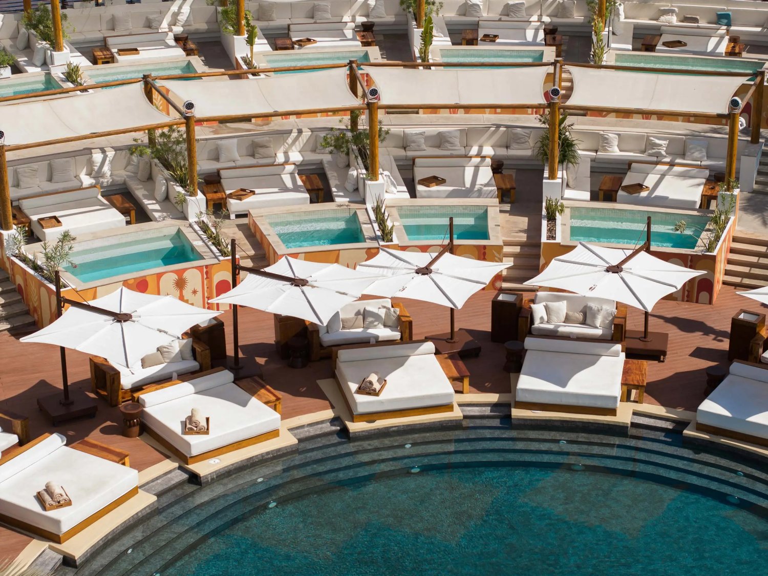 Sun beds with canopys and sofas surrounding the edge of a pool