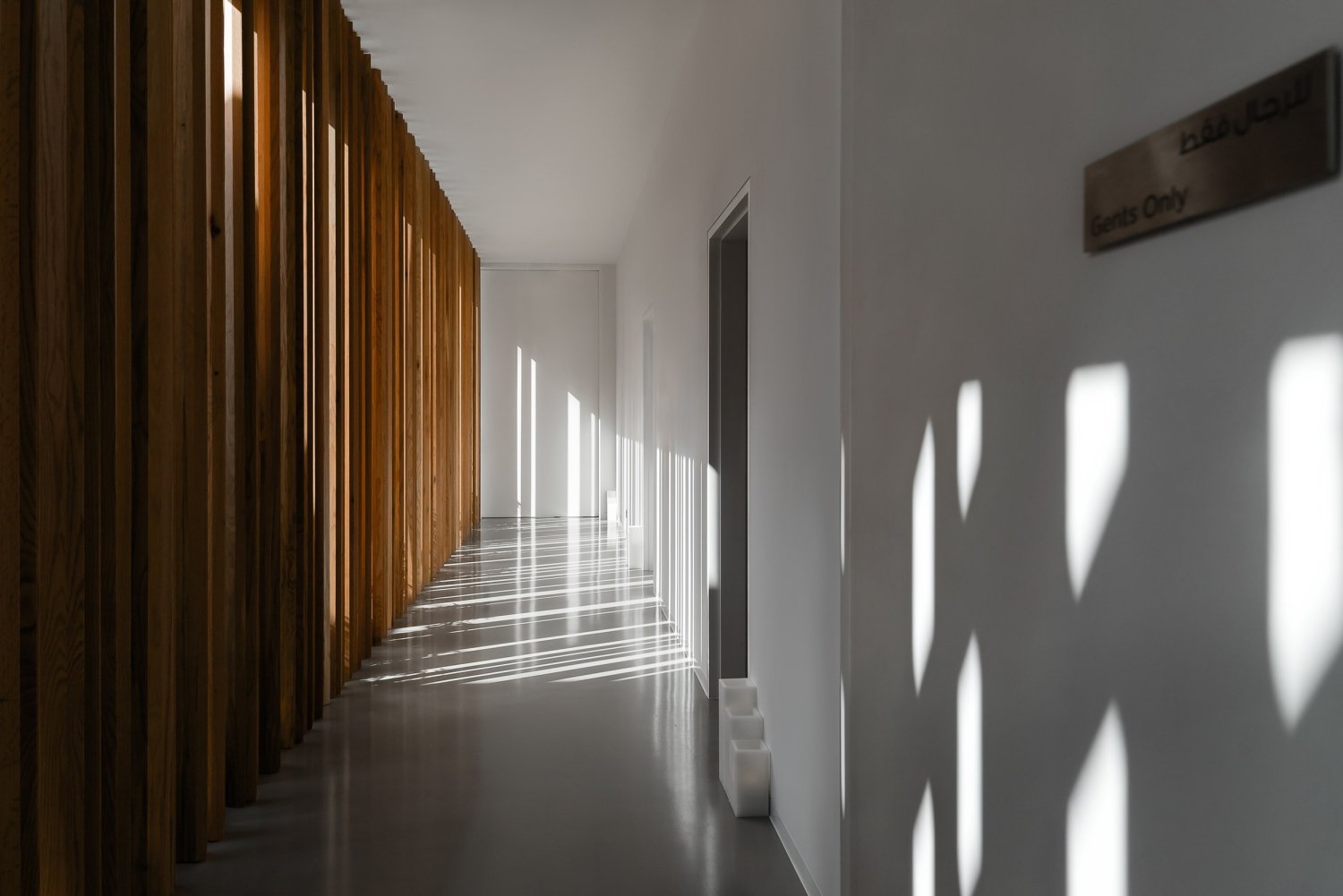 A serene hallway with wooden slats, illuminated by soft light streaming through elegant windows, inviting relaxation