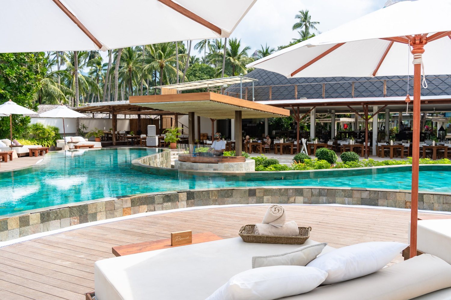 Elegant white lounge chair and umbrella near a sparkling pool, surrounded by tropical gardens at Nikki Beach Koh Samui