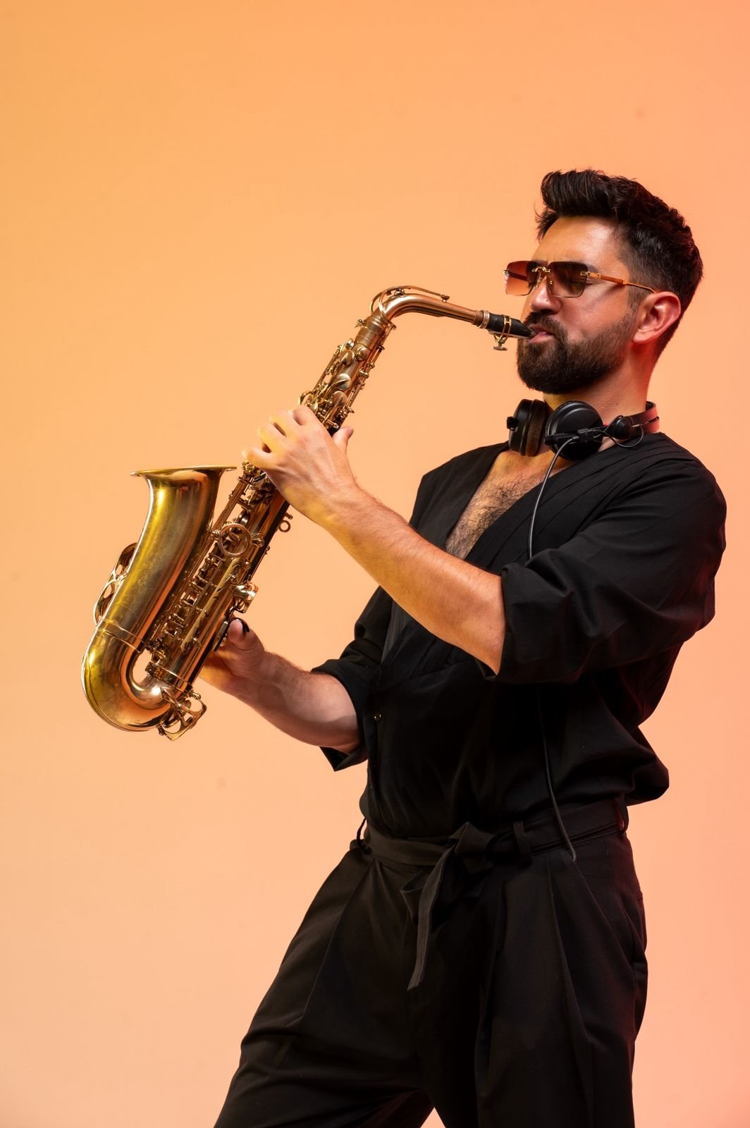 A man in a black shirt and glasses passionately plays the saxophone, embodying the vibrant energy of Nikki Beach Santorini