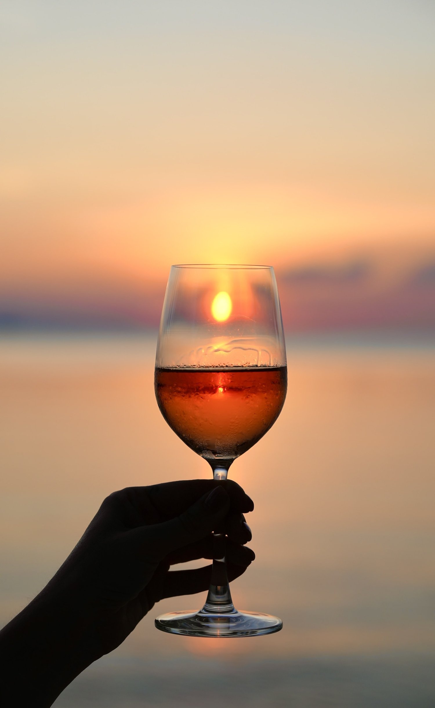 A guest enjoys a glass of wine, silhouetted against a breathtaking Santorini sunset, capturing the essence of summer festivities