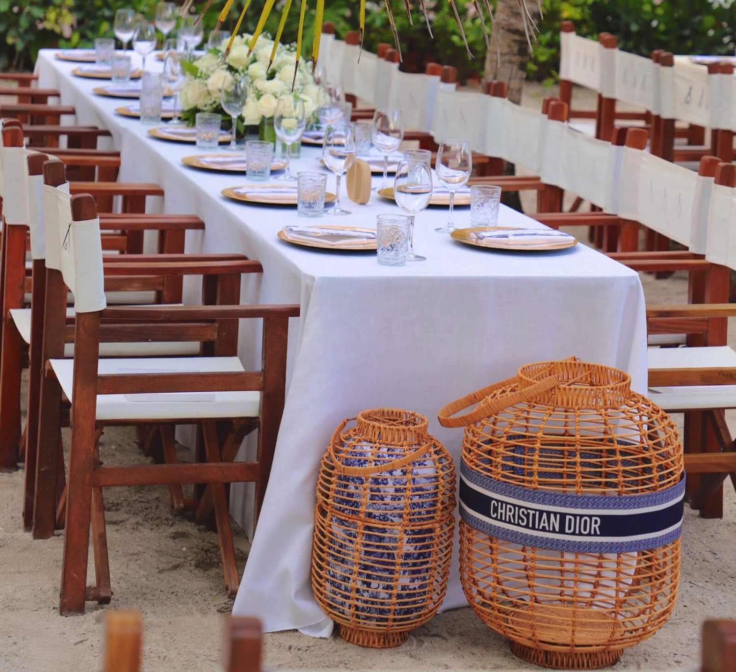 A long dining table set ready for guests, seating approximately 20 people. A Christian Dior wicker basket sits in front of the table