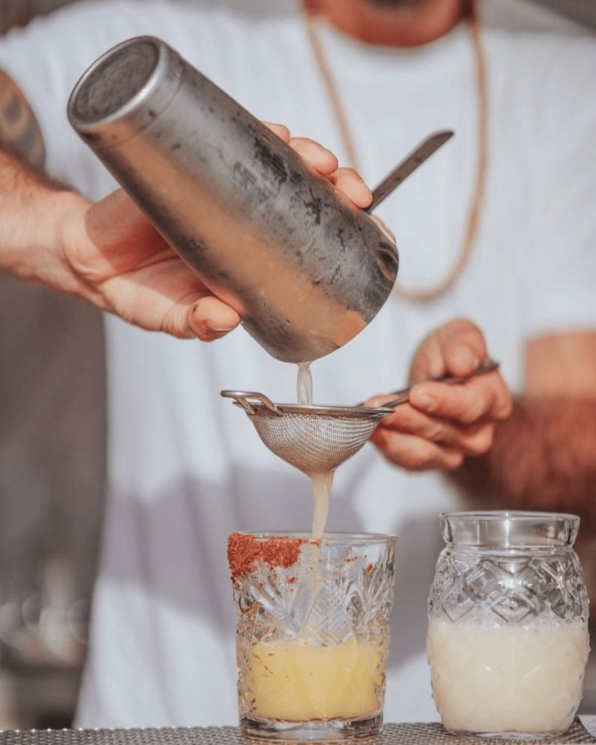 Golden liquid poured through silver mesh, the art of mixology captured mid-motion — every drink a celebration of detail