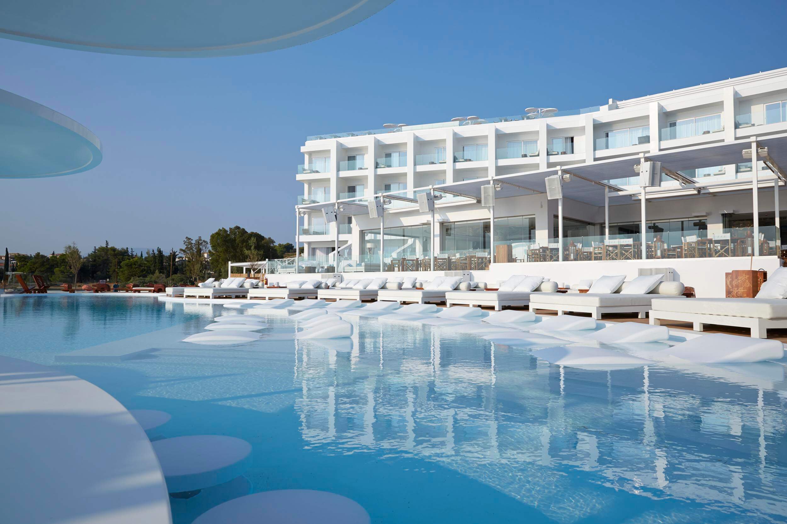 Pool area with sun loungers in the water. Sun beds surround the edge of the pool