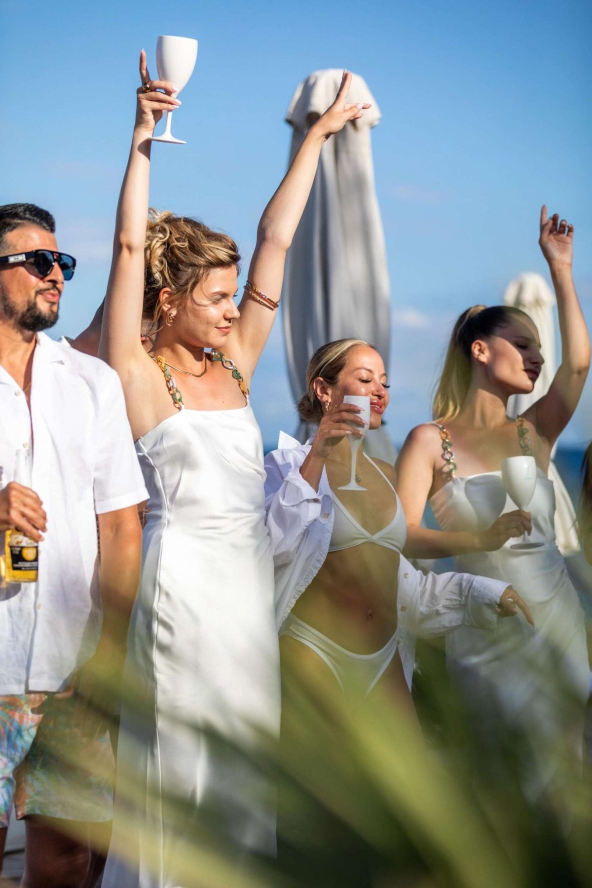 Sunlight dances across white satin as guests lift their glasses to the sky, music in the air and ocean breeze in their hair — the essence of a Santorini celebration