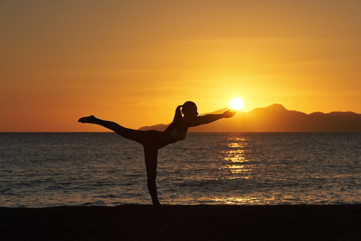 A silhouette poised in perfect balance as the sun sinks into the Aegean — golden light, calm waters, and a moment of pure harmony