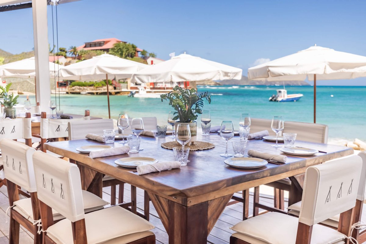 A dining table set out with glasses and tableware looking out over a Caribbean beach