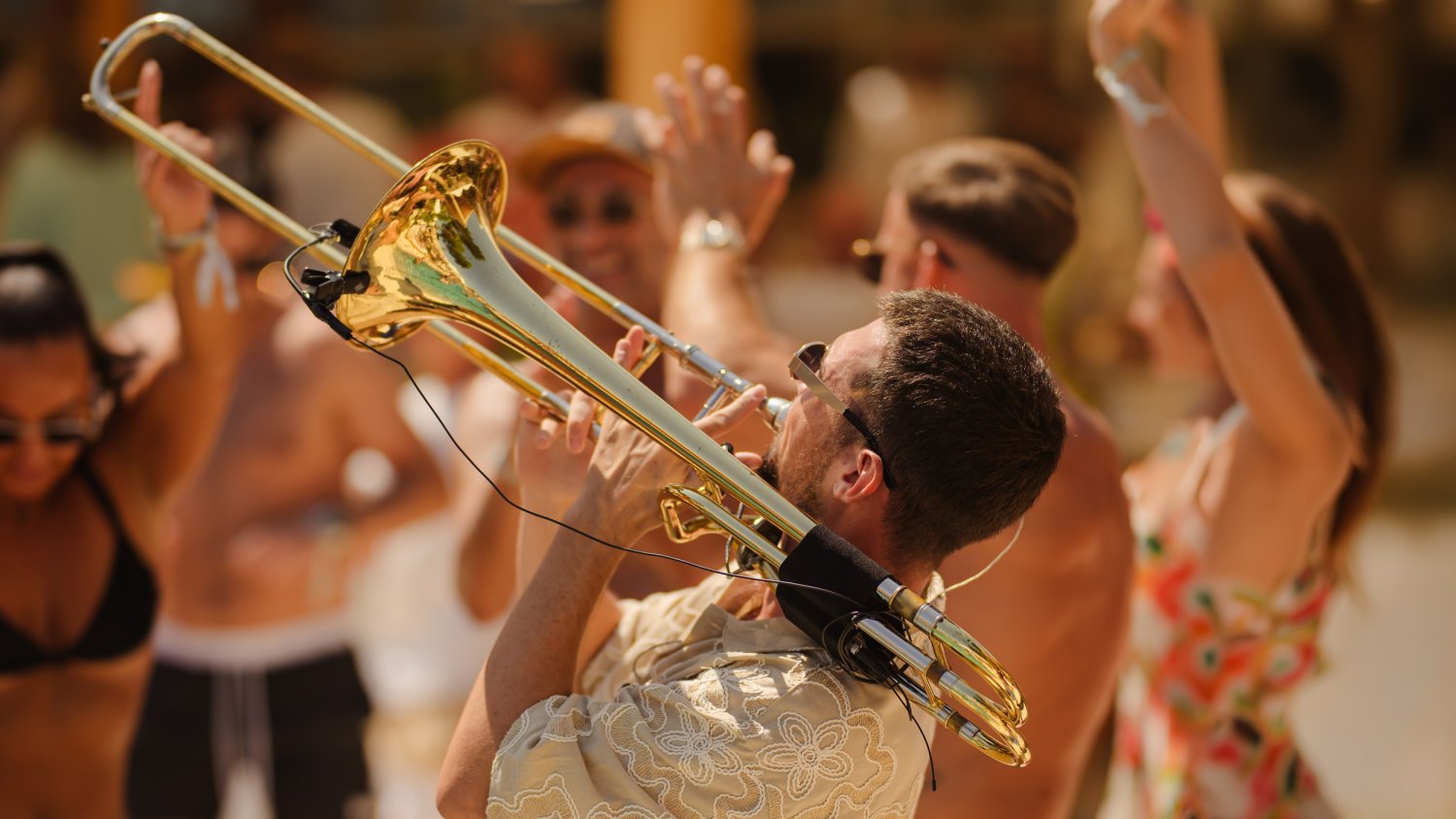 Guy playing the trumpet outside with people dancing around