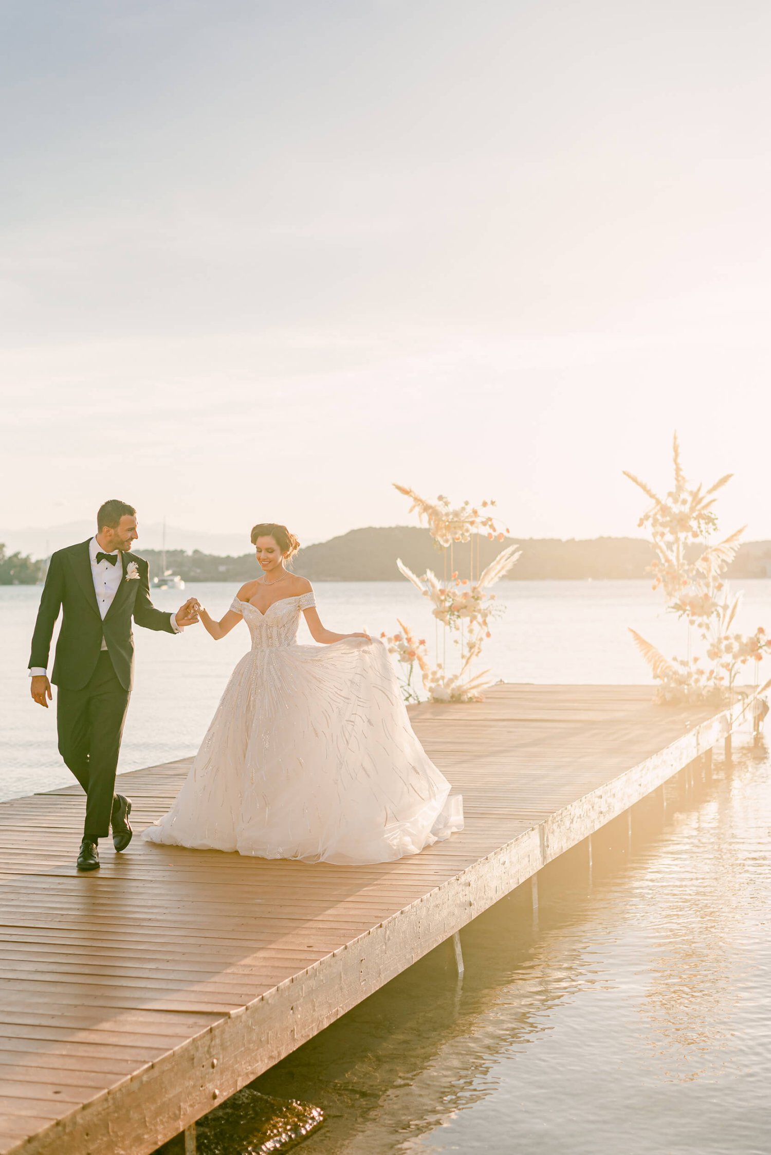 Bride and groom walk hand in hand on a dock at sunset
