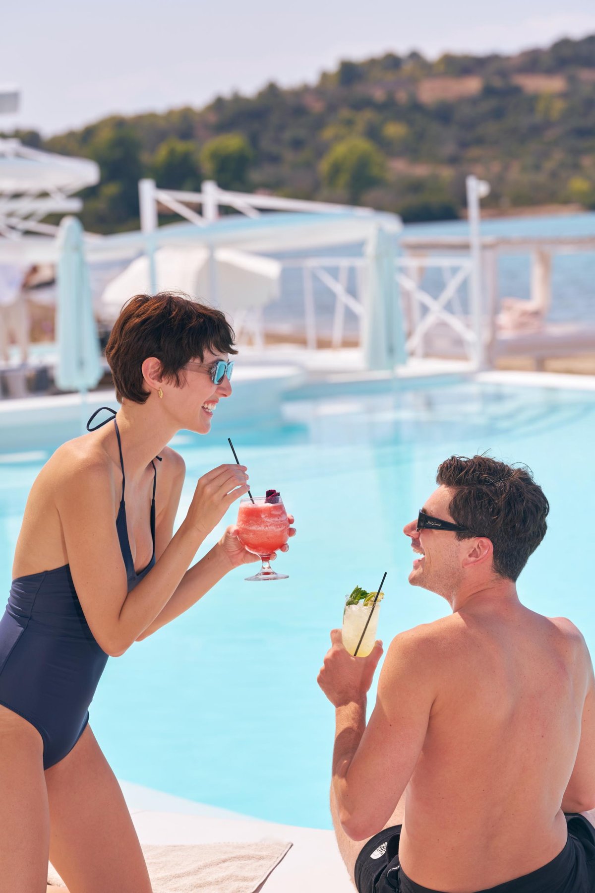 Two people laughing and drinking cocktails by the pool